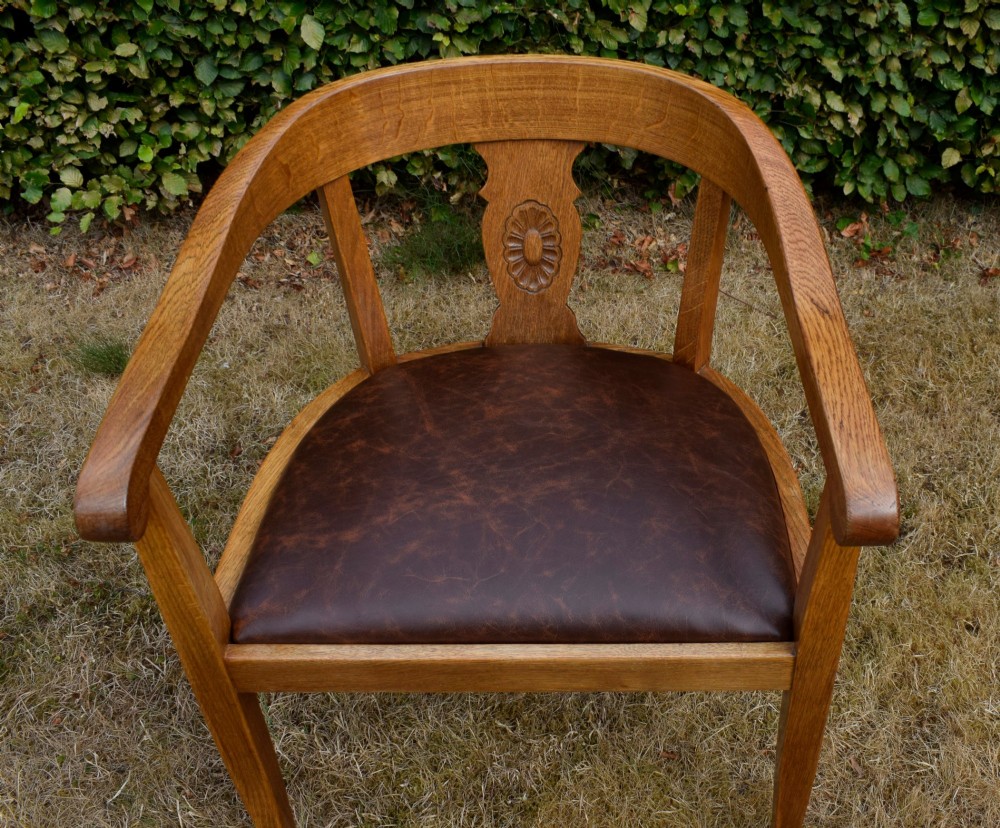 An early 20th-century oak desk chair featuring a curved horseshoe backrest, a carved central splat, and a dark brown upholstered seat pad. View XIV
