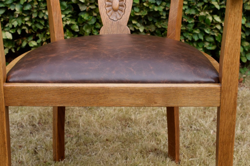 An early 20th-century oak desk chair featuring a curved horseshoe backrest, a carved central splat, and a dark brown upholstered seat pad. View XV