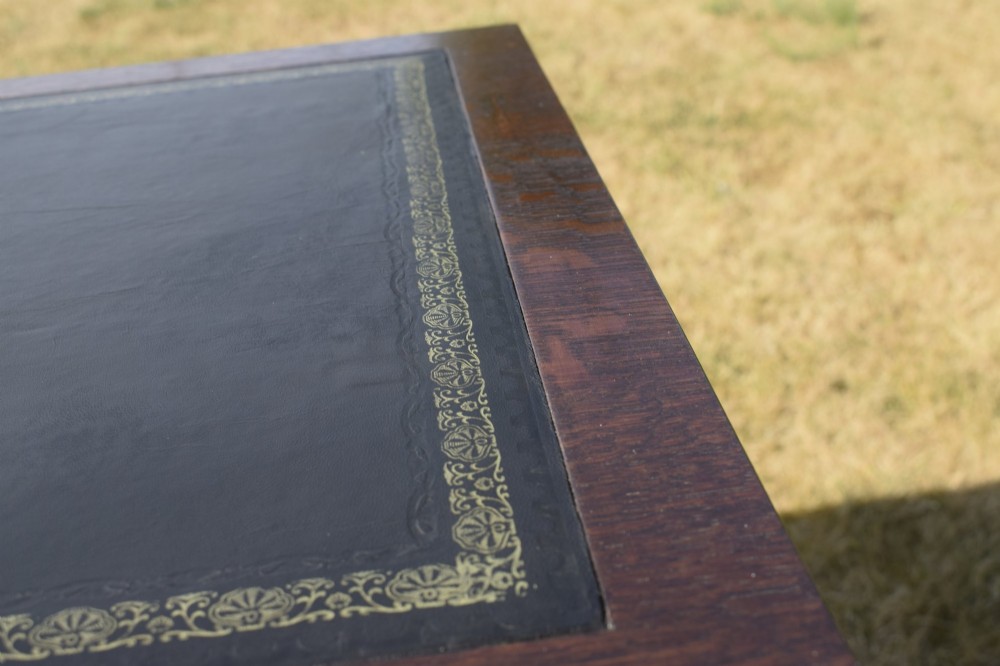 A warm brown oak Arts and Crafts writing desk with a dark inset leather top, a single drawer with turned wooden knobs, and four square straight legs. View X