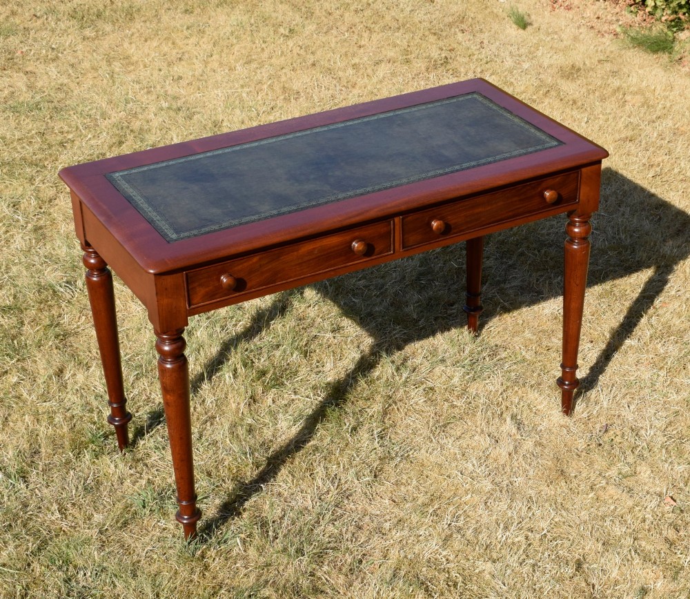 A Victorian mahogany writing desk featuring a green leather inset top with gold tooling, two frieze drawers with turned knob handles, and four slender turned legs.