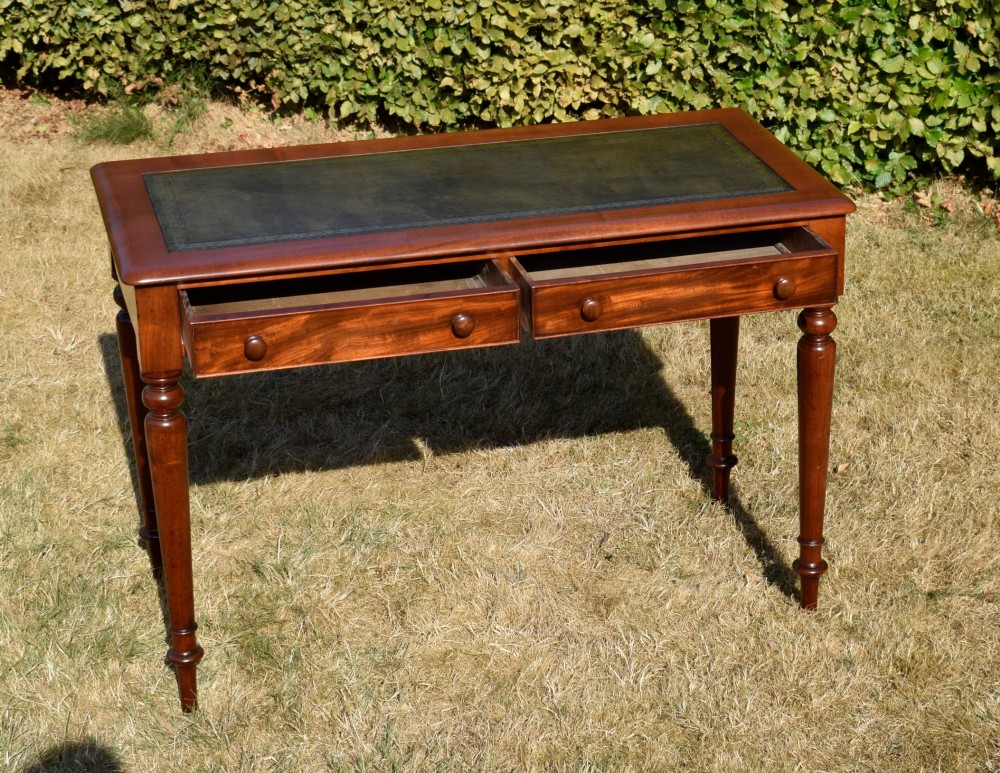 A Victorian mahogany writing desk featuring a green leather inset top with gold tooling, two frieze drawers with turned knob handles, and four slender turned legs. View X