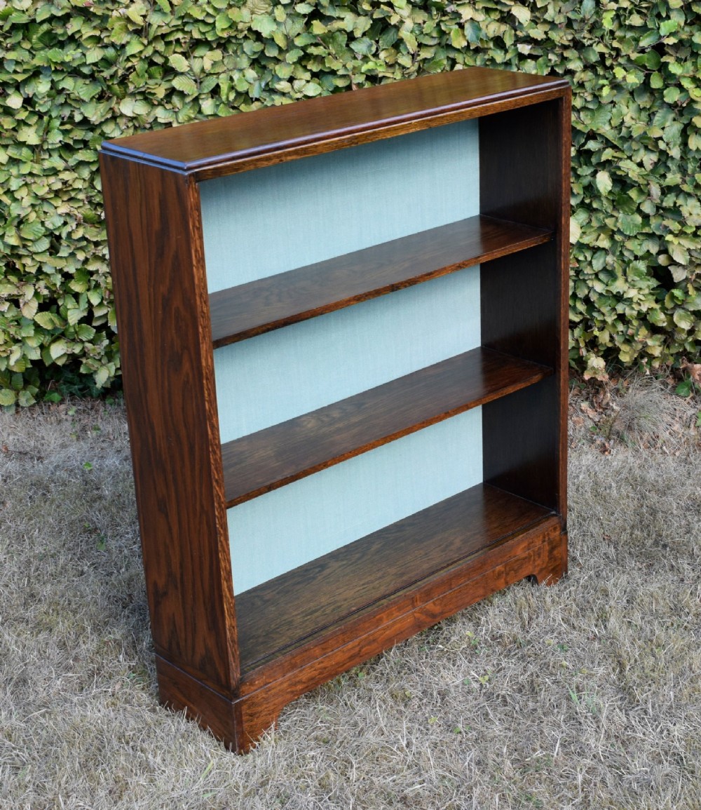 A dark oak Art Deco open bookcase featuring three shelves and a light duck-egg blue textured back panel.
