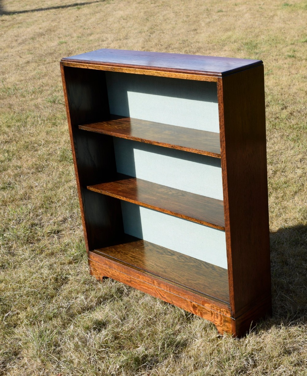 A dark oak Art Deco open bookcase featuring three shelves and a light duck-egg blue textured back panel. View III
