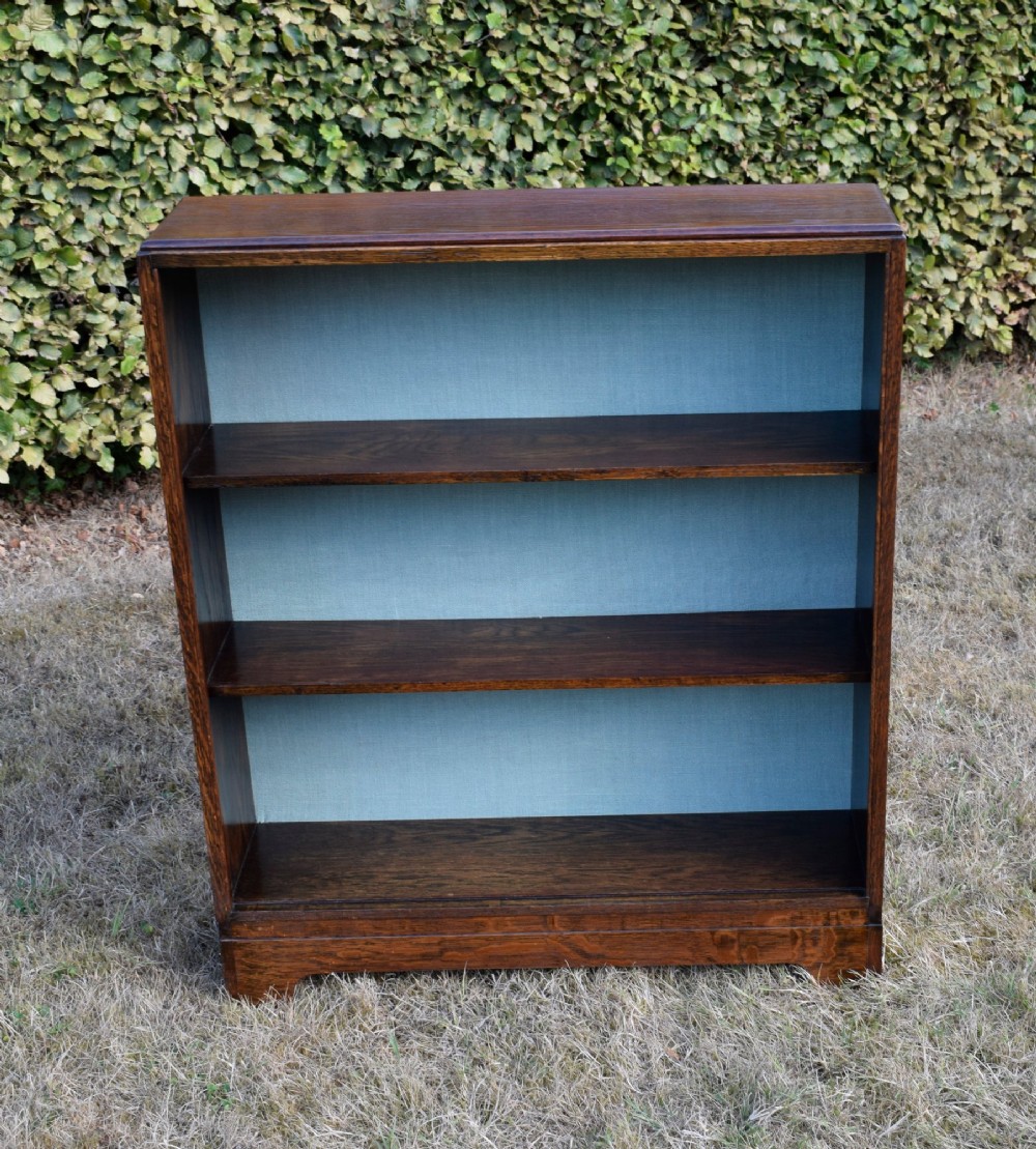 A dark oak Art Deco open bookcase featuring three shelves and a light duck-egg blue textured back panel. View VII