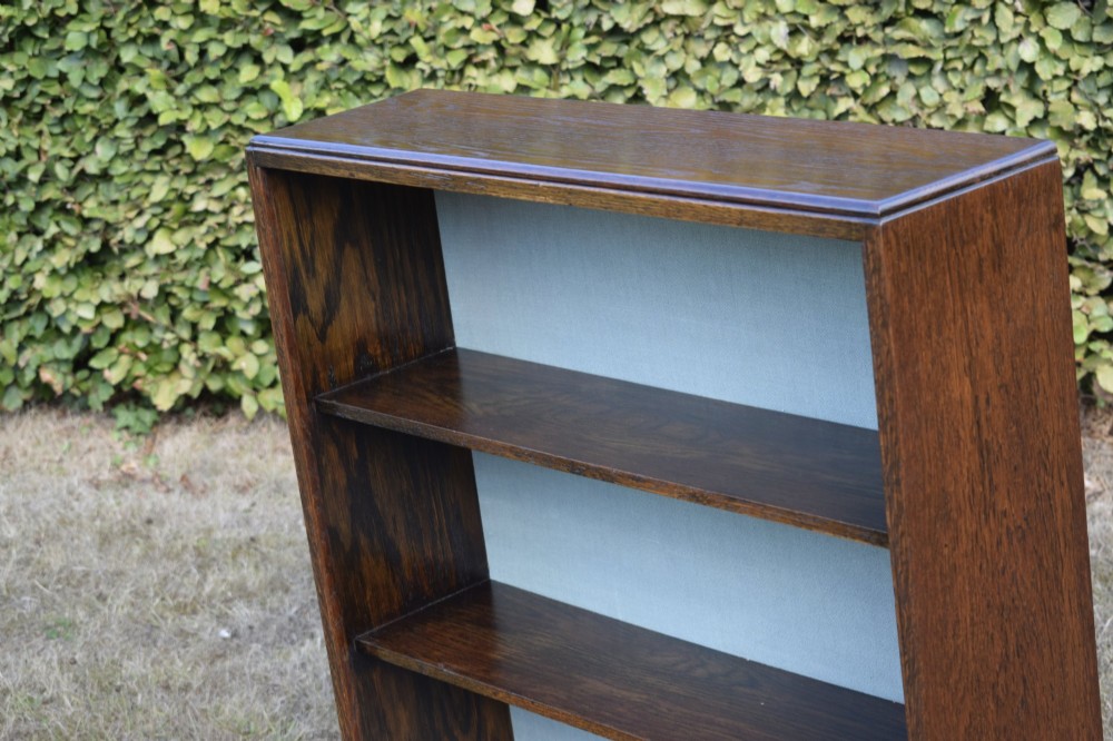 A dark oak Art Deco open bookcase featuring three shelves and a light duck-egg blue textured back panel. View IX
