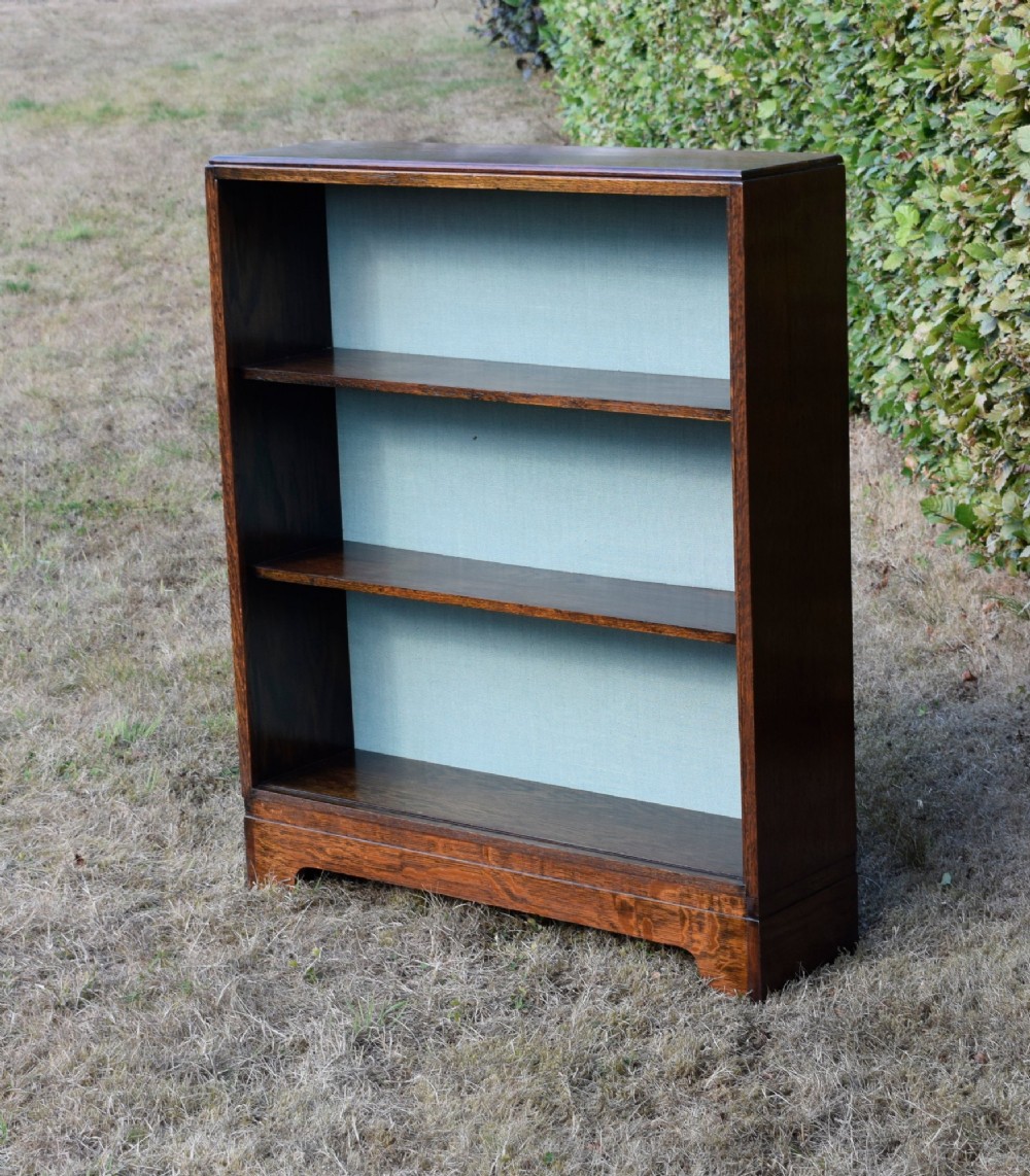 A dark oak Art Deco open bookcase featuring three shelves and a light duck-egg blue textured back panel. View XIII