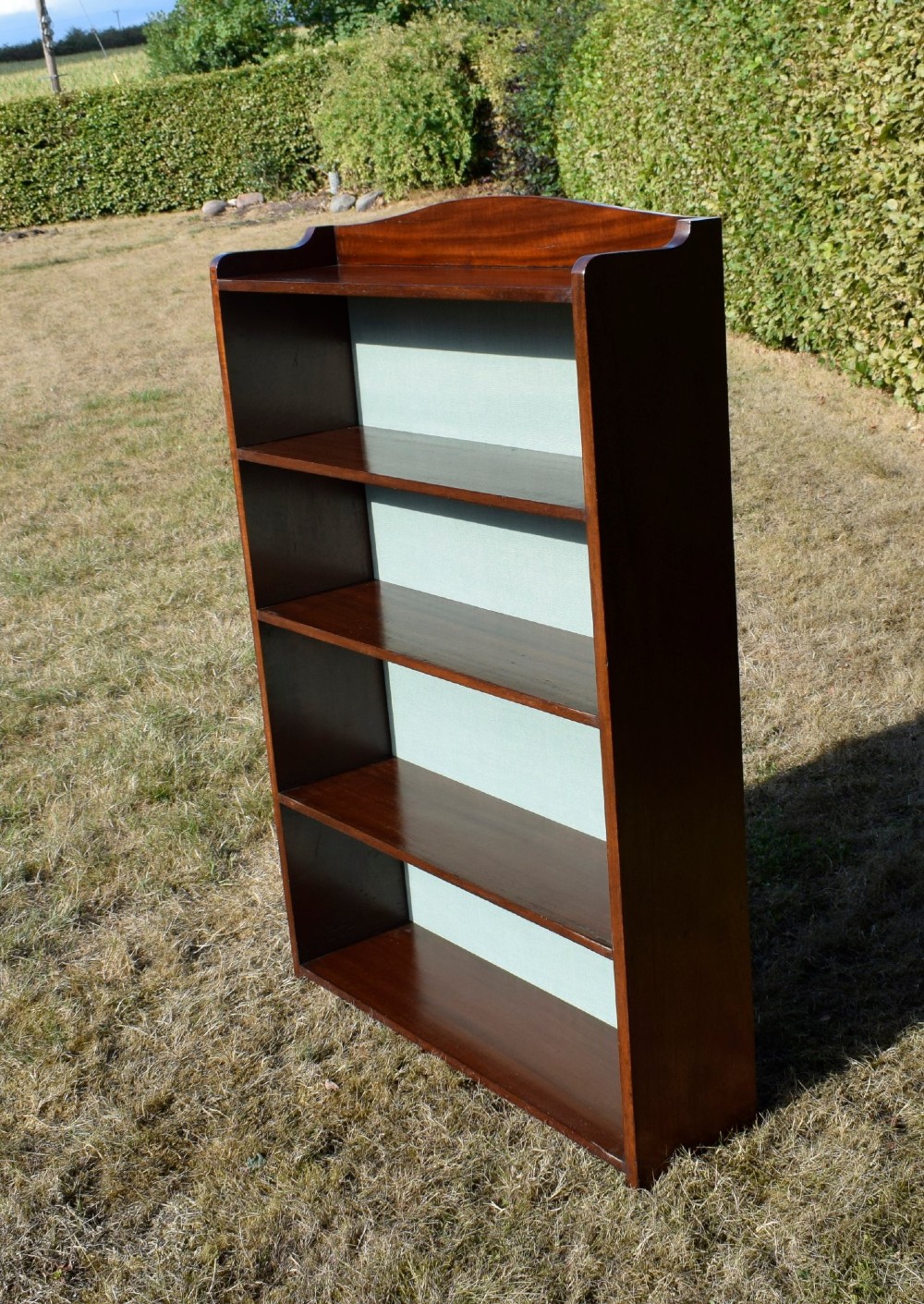 A standing mahogany open bookcase featuring four horizontal shelves, a gently curved top upstand, and a light-coloured fabric back panel. View II