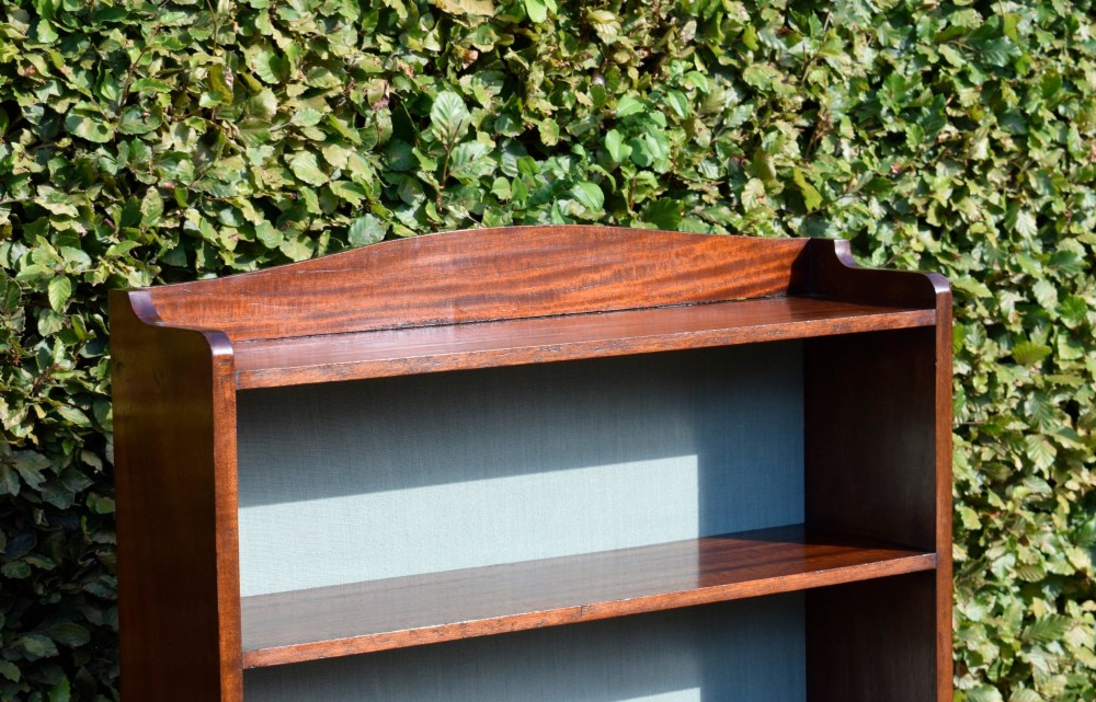 A standing mahogany open bookcase featuring four horizontal shelves, a gently curved top upstand, and a light-coloured fabric back panel. View VI