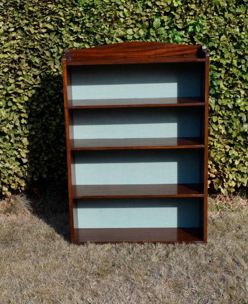 A standing mahogany open bookcase featuring four horizontal shelves, a gently curved top upstand, and a light-coloured fabric back panel. View VII