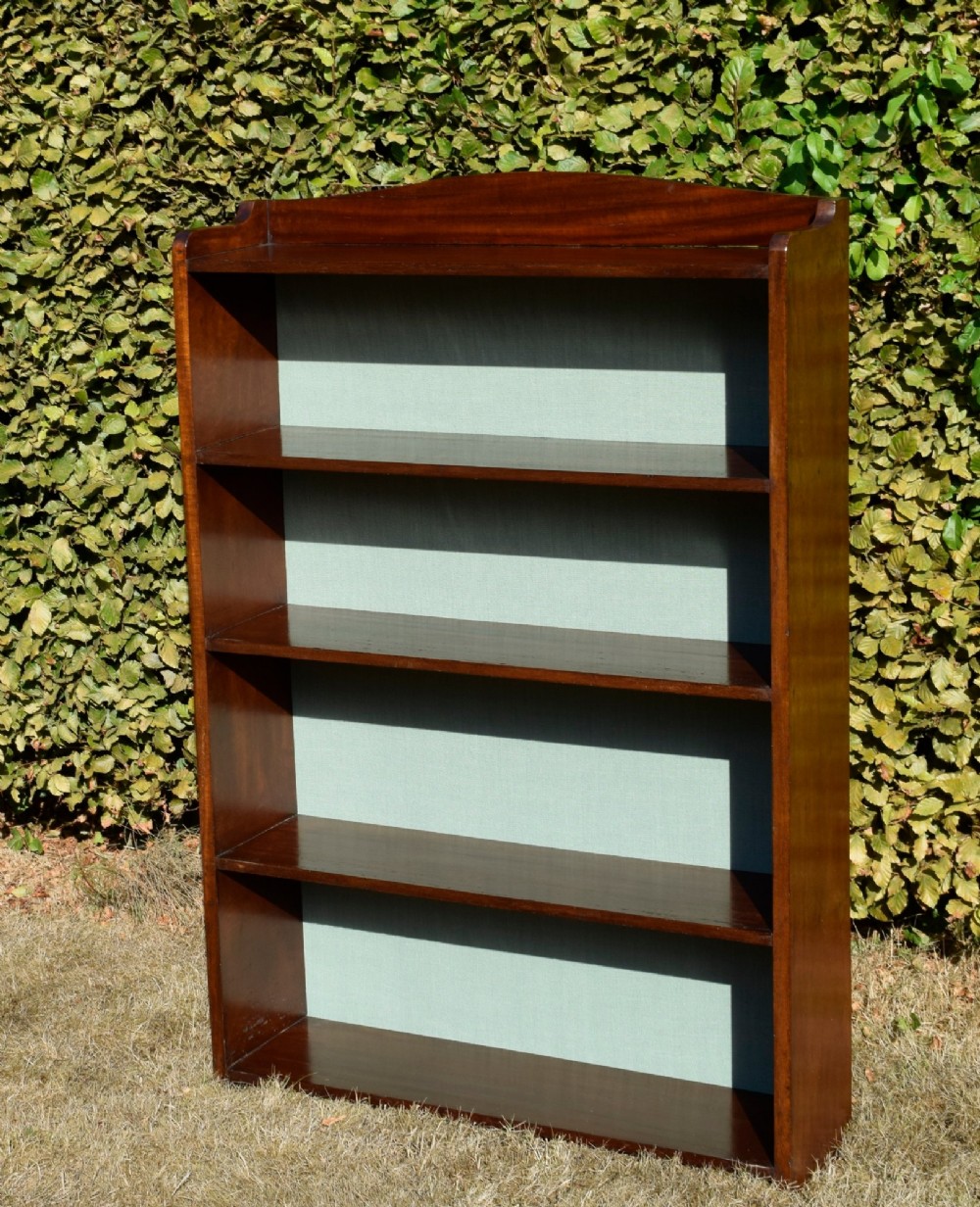 A standing mahogany open bookcase featuring four horizontal shelves, a gently curved top upstand, and a light-coloured fabric back panel. View VIII