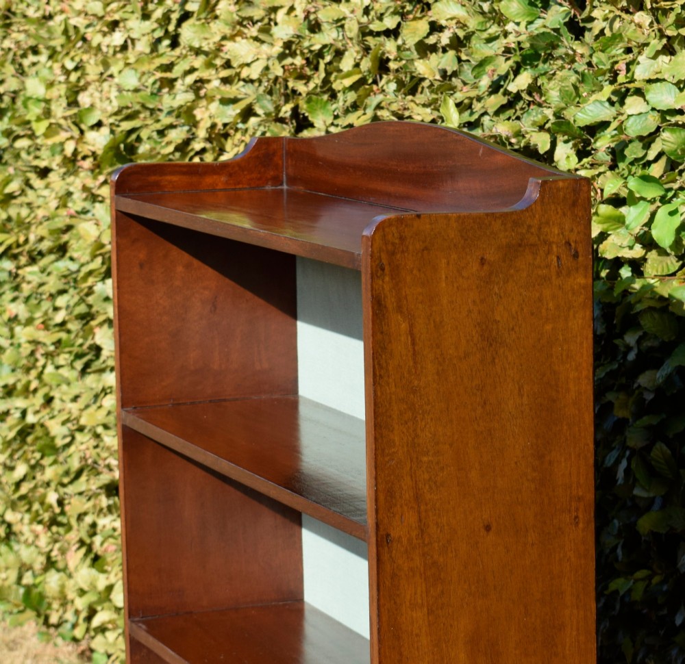 A standing mahogany open bookcase featuring four horizontal shelves, a gently curved top upstand, and a light-coloured fabric back panel. View XI