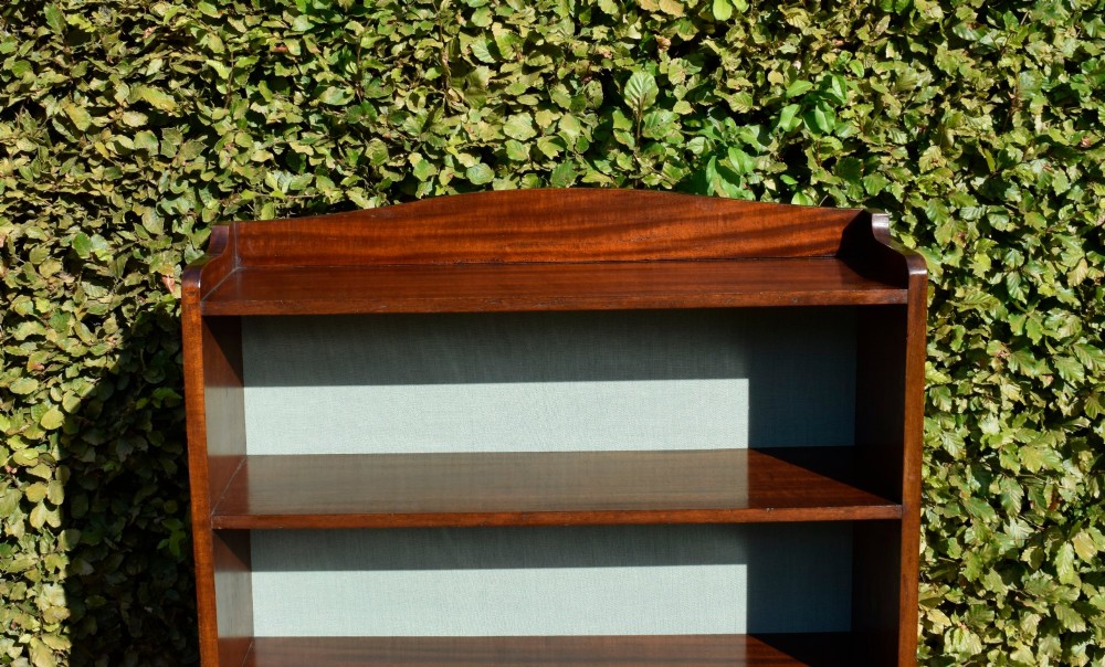A standing mahogany open bookcase featuring four horizontal shelves, a gently curved top upstand, and a light-coloured fabric back panel. View XII