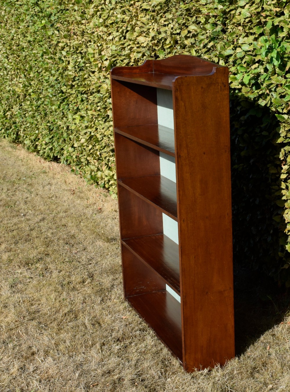 A standing mahogany open bookcase featuring four horizontal shelves, a gently curved top upstand, and a light-coloured fabric back panel. View XIII