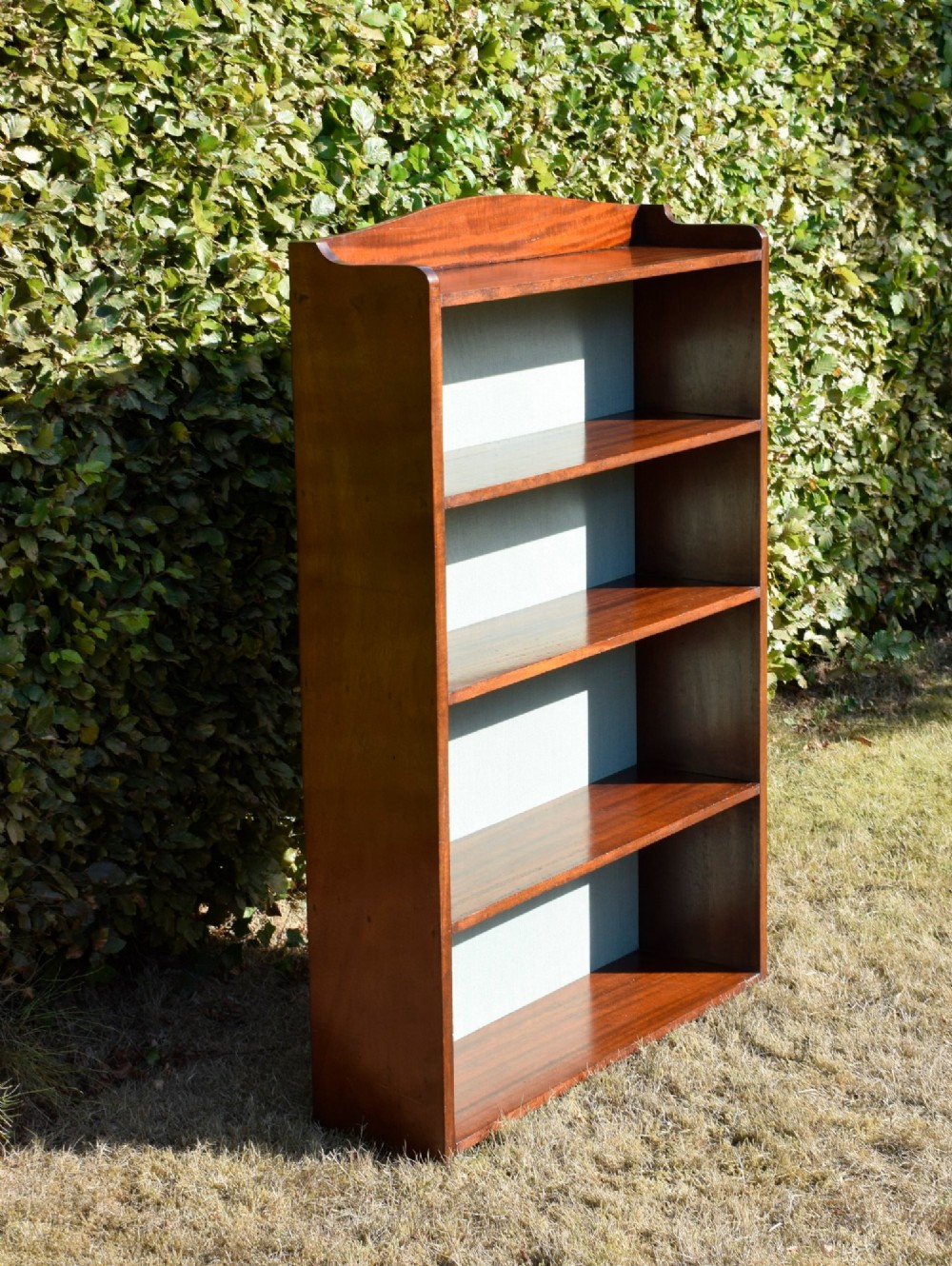 A standing mahogany open bookcase featuring four horizontal shelves, a gently curved top upstand, and a light-coloured fabric back panel. View XIV