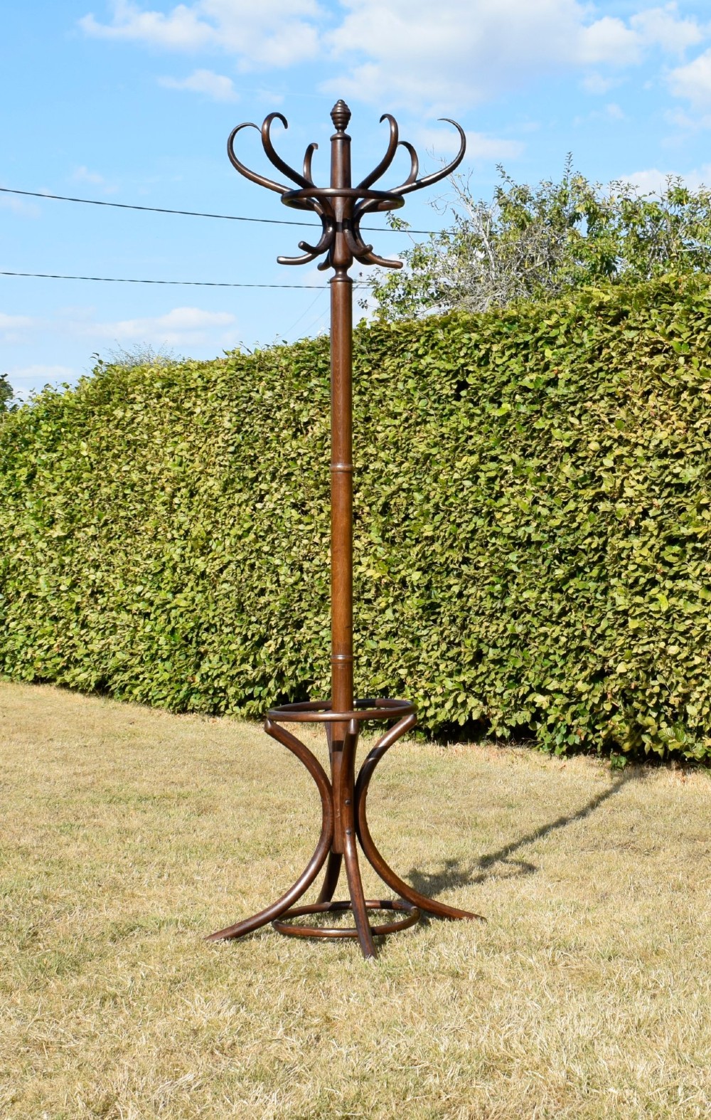 A dark brown bentwood coat and hat stand featuring curved upper hooks, a turned central post, an umbrella ring, and curved tripod legs.