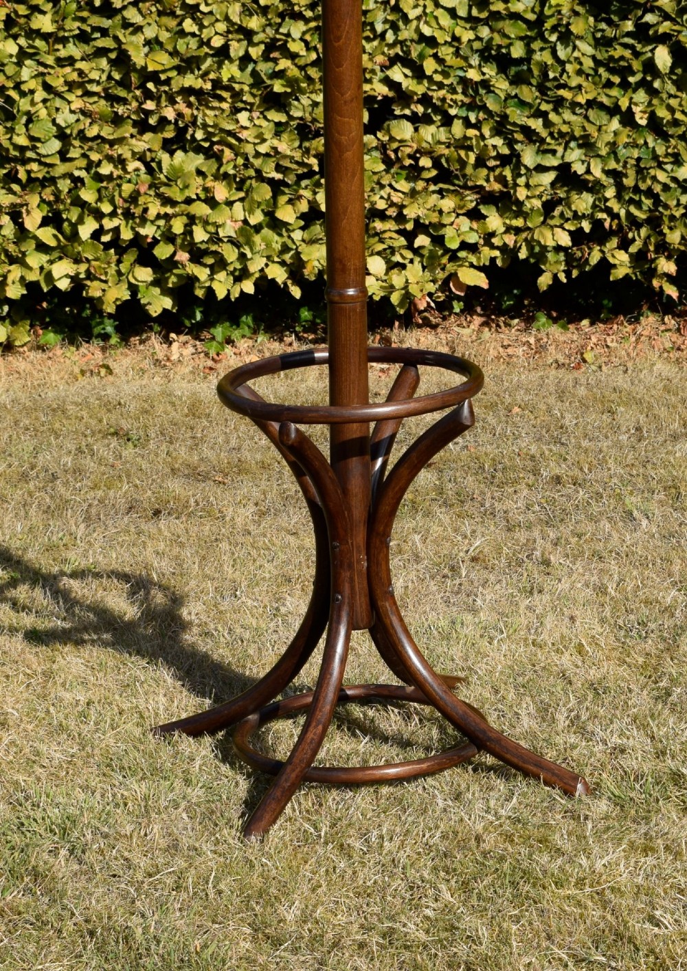 A dark brown bentwood coat and hat stand featuring curved upper hooks, a turned central post, an umbrella ring, and curved tripod legs. View V