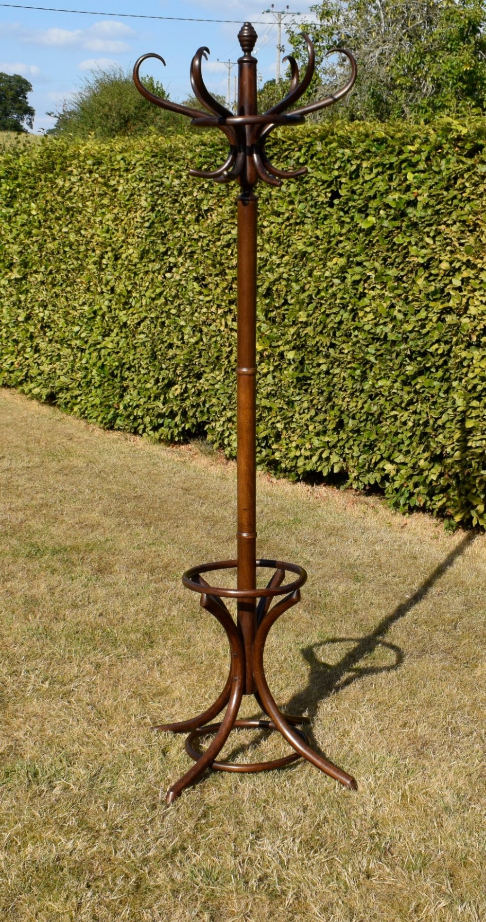 A dark brown bentwood coat and hat stand featuring curved upper hooks, a turned central post, an umbrella ring, and curved tripod legs. View XI