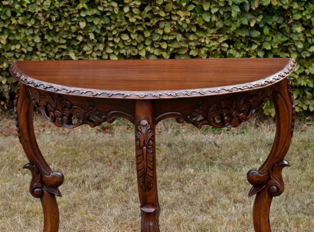 A dark mahogany demi-lune console table featuring deep acanthus leaf carvings on the frieze and three cabriole legs. View II
