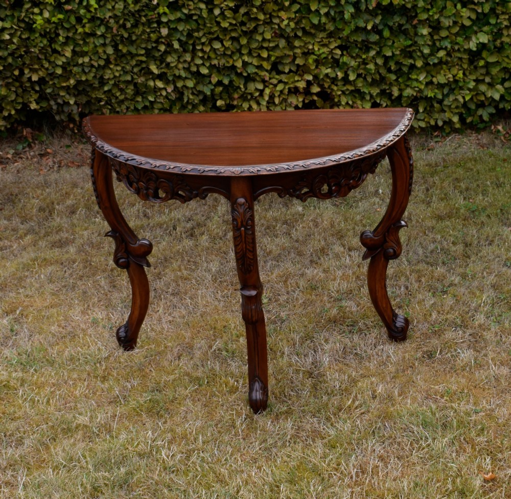 A dark mahogany demi-lune console table featuring deep acanthus leaf carvings on the frieze and three cabriole legs. View VI