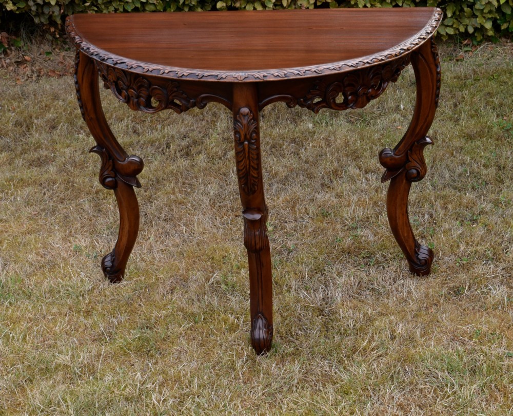 A dark mahogany demi-lune console table featuring deep acanthus leaf carvings on the frieze and three cabriole legs. View VII
