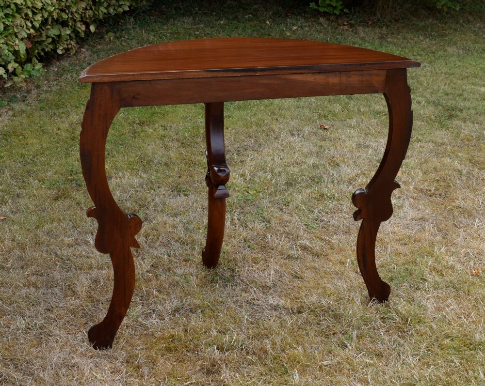 A dark mahogany demi-lune console table featuring deep acanthus leaf carvings on the frieze and three cabriole legs. View X