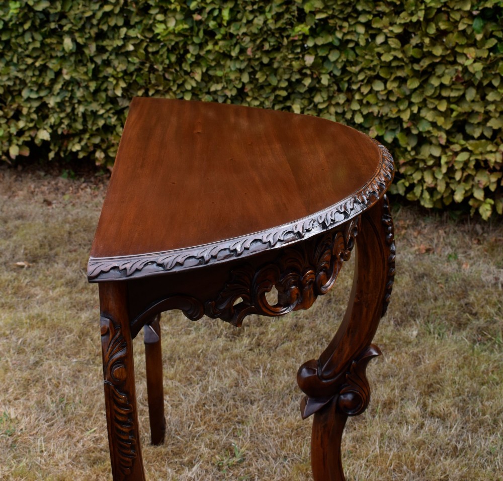 A dark mahogany demi-lune console table featuring deep acanthus leaf carvings on the frieze and three cabriole legs. View XI