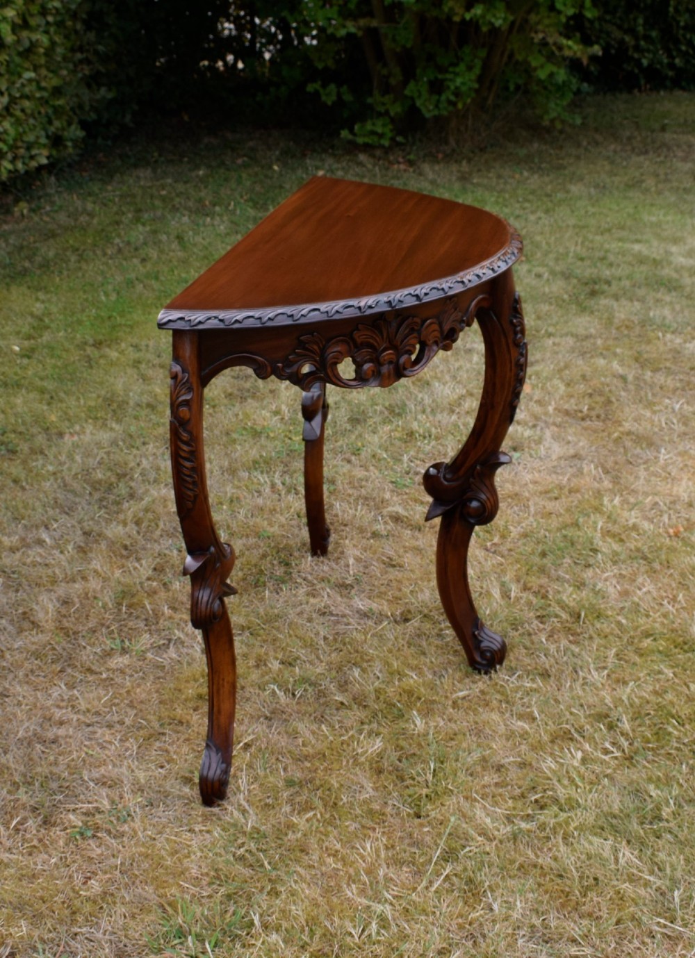 A dark mahogany demi-lune console table featuring deep acanthus leaf carvings on the frieze and three cabriole legs. View XII