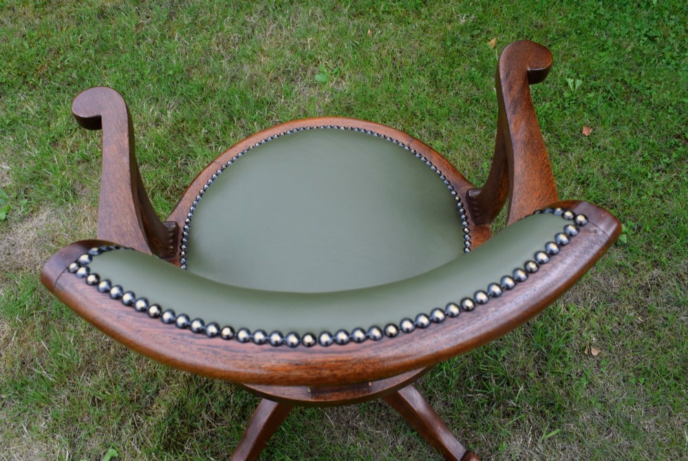 An early 20th-century oak swivel desk chair featuring a green leather padded seat and backrest trimmed with metal studs, supported by a four-spoke wooden base with a central iron mechanism. View VIII