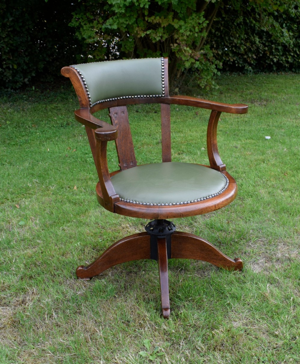 An early 20th-century oak swivel desk chair featuring a green leather padded seat and backrest trimmed with metal studs, supported by a four-spoke wooden base with a central iron mechanism. View XI