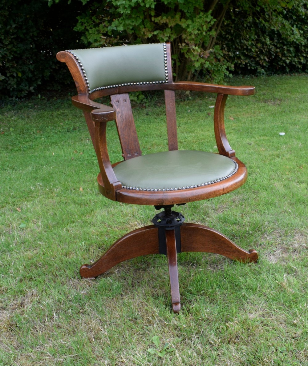An early 20th-century oak swivel desk chair featuring a green leather padded seat and backrest trimmed with metal studs, supported by a four-spoke wooden base with a central iron mechanism. View XII