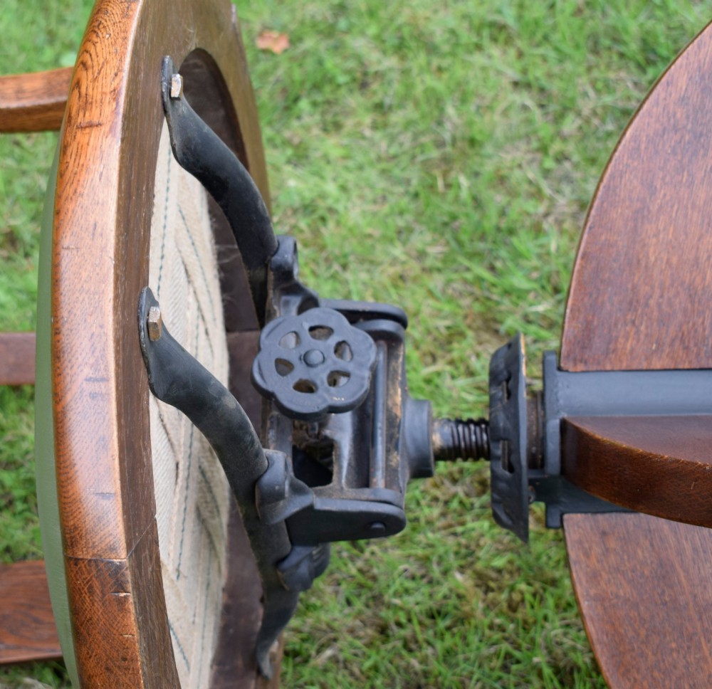 An early 20th-century oak swivel desk chair featuring a green leather padded seat and backrest trimmed with metal studs, supported by a four-spoke wooden base with a central iron mechanism. View XV