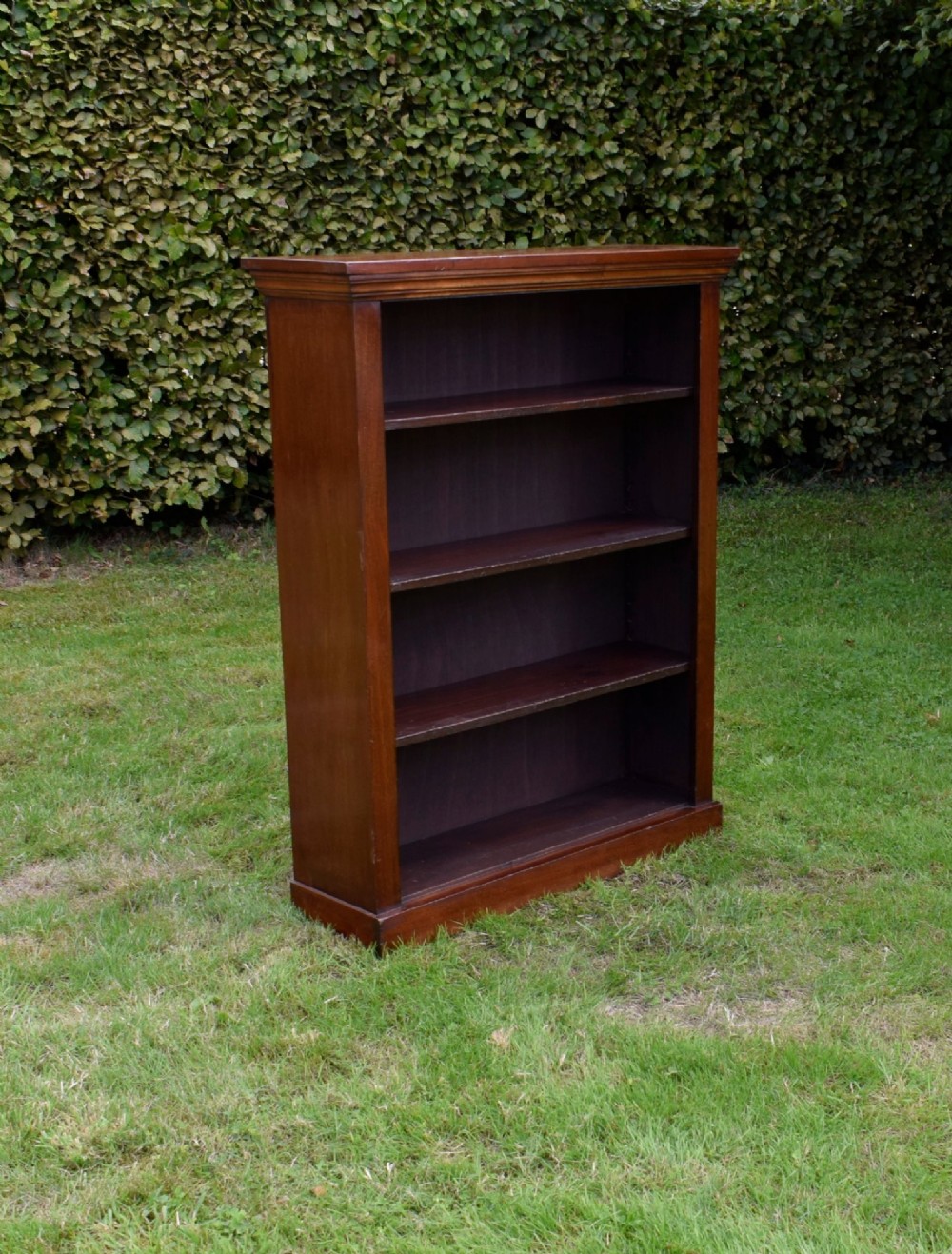 An early 20th-century open-front mahogany bookcase featuring three internal shelves, a moulded top cornice, and a sturdy plinth base.