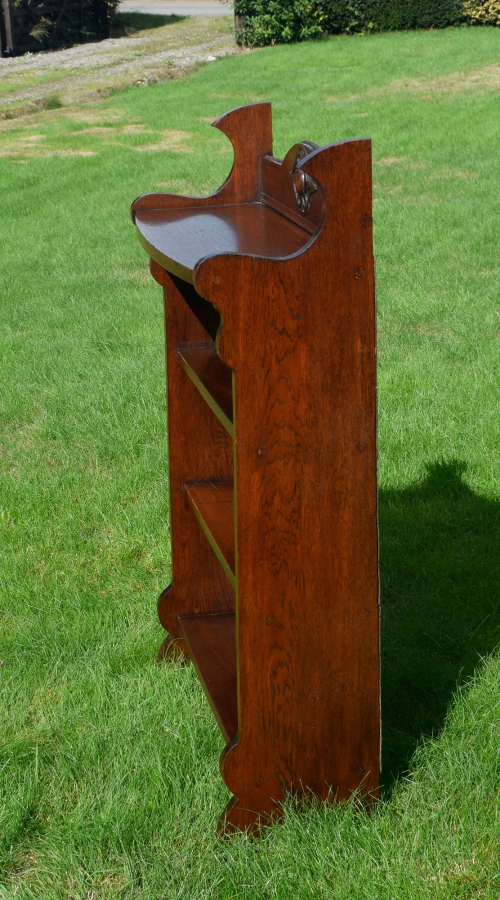 An early twentieth-century open oak bookcase featuring a carved floral crest on the top gallery, shaped sides, and three fixed shelves. View VI