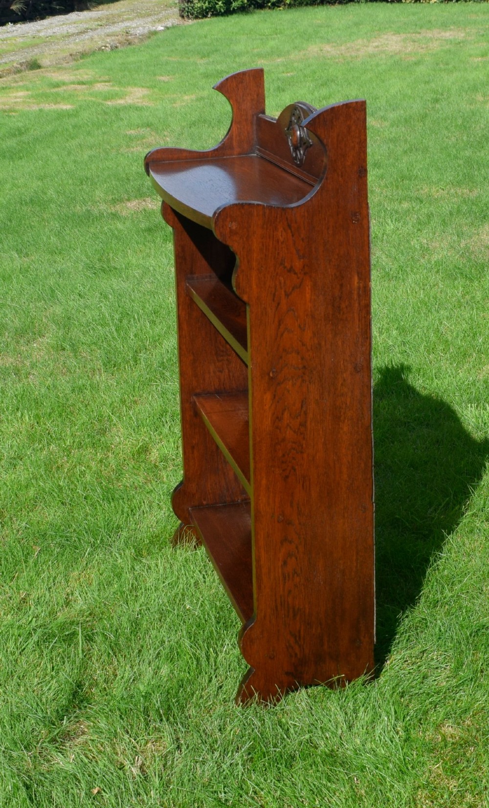 An early twentieth-century open oak bookcase featuring a carved floral crest on the top gallery, shaped sides, and three fixed shelves. View VIII