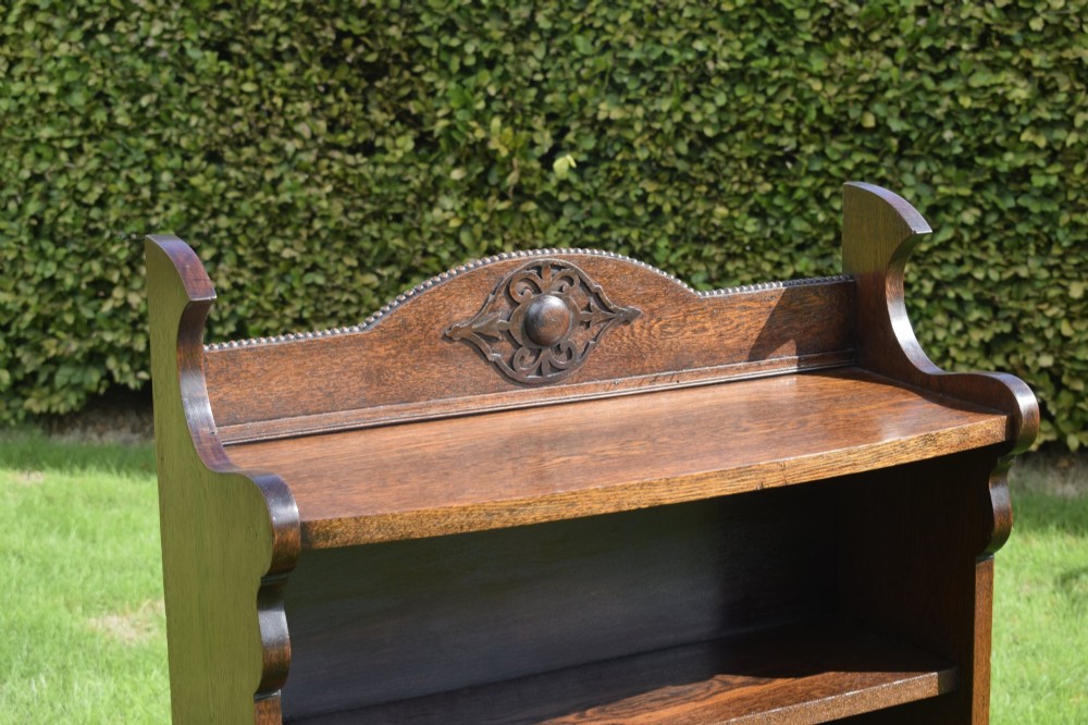 An early twentieth-century open oak bookcase featuring a carved floral crest on the top gallery, shaped sides, and three fixed shelves. View IX