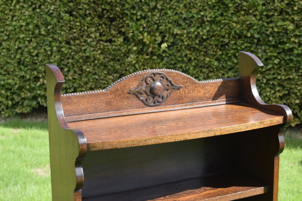 An early twentieth-century open oak bookcase featuring a carved floral crest on the top gallery, shaped sides, and three fixed shelves. View X