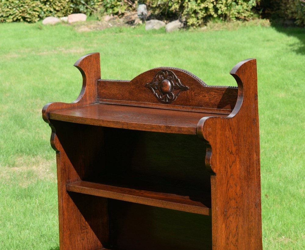 An early twentieth-century open oak bookcase featuring a carved floral crest on the top gallery, shaped sides, and three fixed shelves. View XII