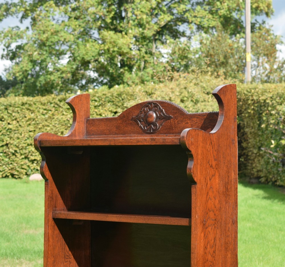 An early twentieth-century open oak bookcase featuring a carved floral crest on the top gallery, shaped sides, and three fixed shelves. View XIII