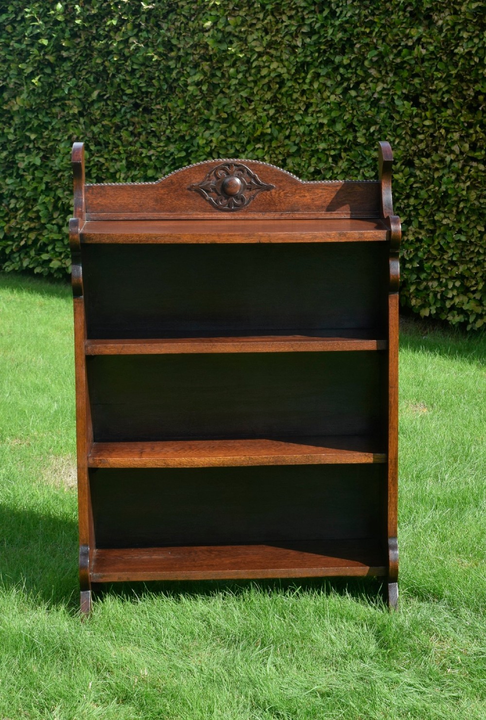 An early twentieth-century open oak bookcase featuring a carved floral crest on the top gallery, shaped sides, and three fixed shelves. View XIV