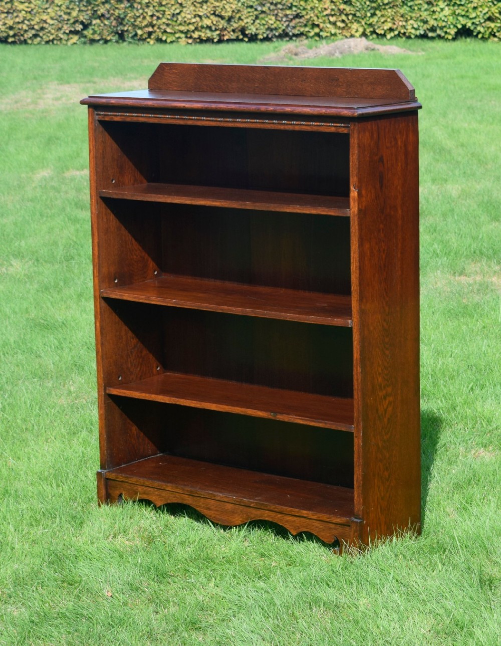 An early 20th-century open dark oak bookcase with four shelves, a low top gallery, and a scalloped plinth base.