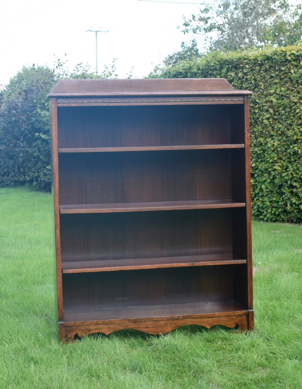 An early 20th-century open dark oak bookcase with four shelves, a low top gallery, and a scalloped plinth base. View V