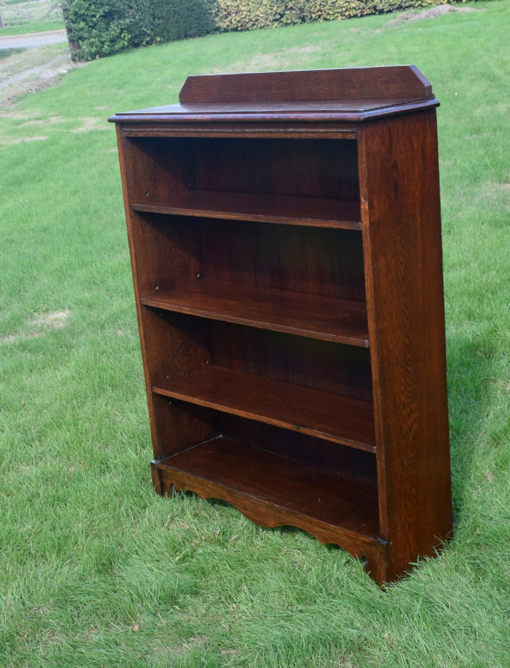 An early 20th-century open dark oak bookcase with four shelves, a low top gallery, and a scalloped plinth base. View VII
