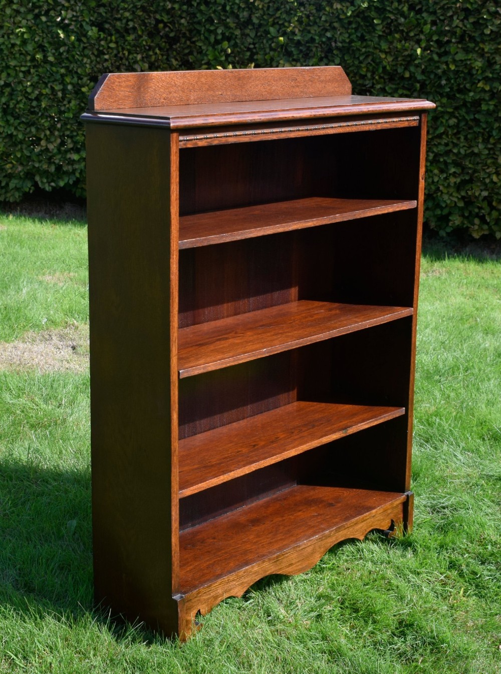 An early 20th-century open dark oak bookcase with four shelves, a low top gallery, and a scalloped plinth base. View X