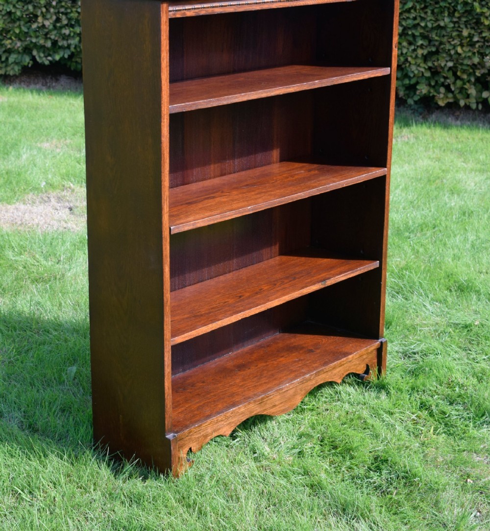 An early 20th-century open dark oak bookcase with four shelves, a low top gallery, and a scalloped plinth base. View XI