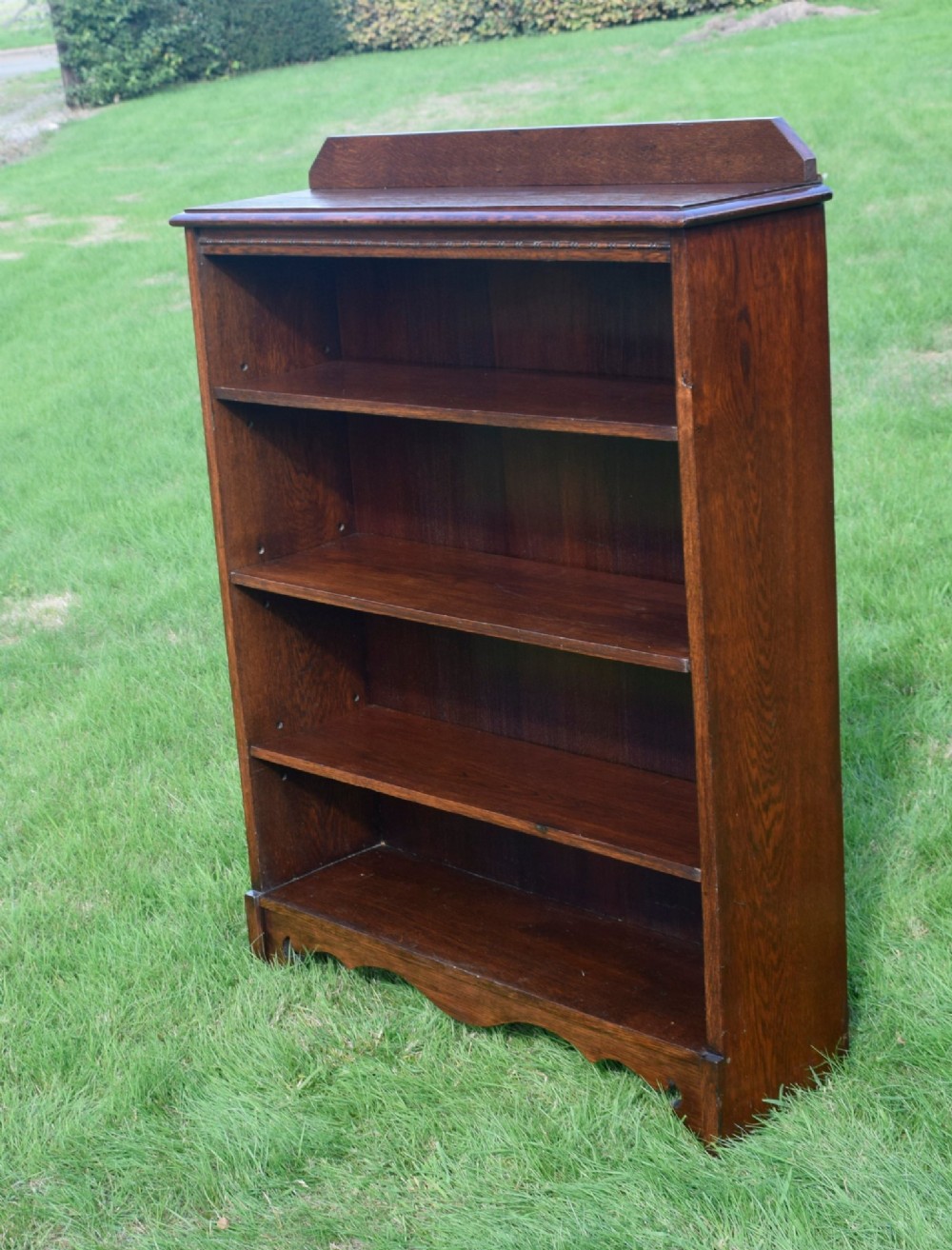 An early 20th-century open dark oak bookcase with four shelves, a low top gallery, and a scalloped plinth base. View XII