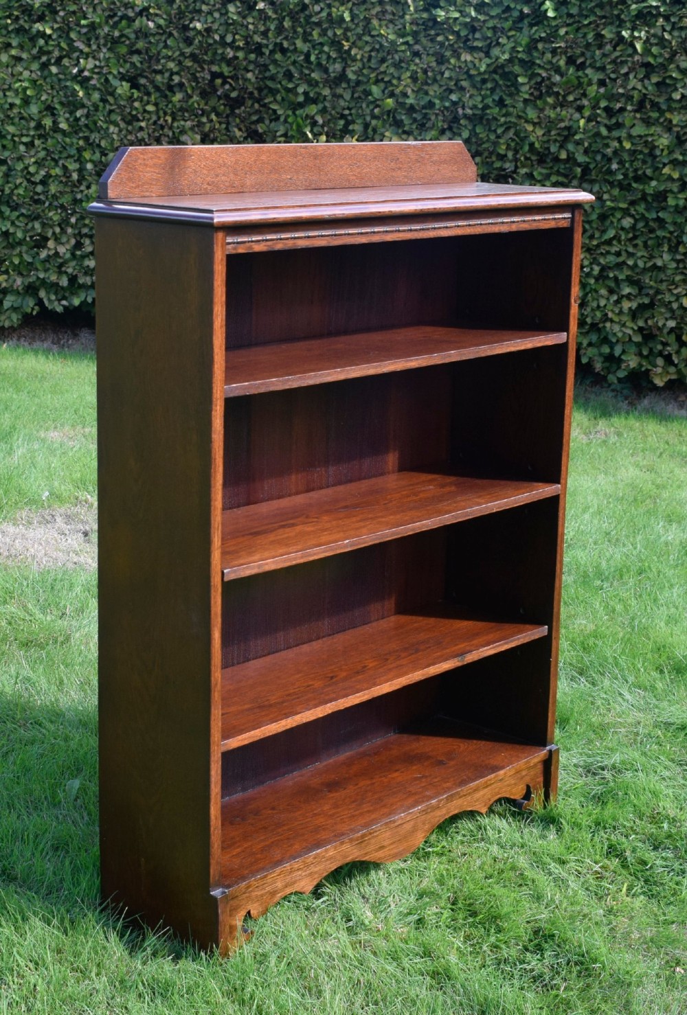 An early 20th-century open dark oak bookcase with four shelves, a low top gallery, and a scalloped plinth base. View XIII