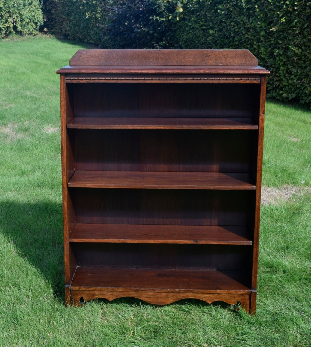 An early 20th-century open dark oak bookcase with four shelves, a low top gallery, and a scalloped plinth base. View XIV