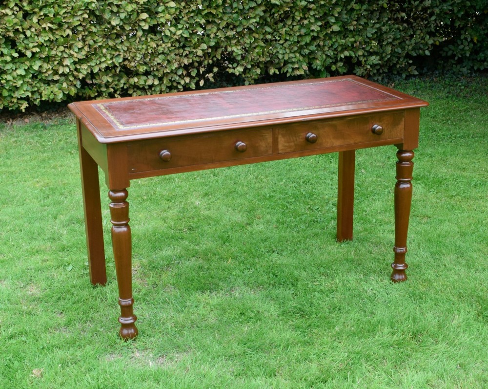 A Victorian mahogany writing table with a red leather inset surface, two drawers with wooden knob handles, turned front legs, and square back legs.
