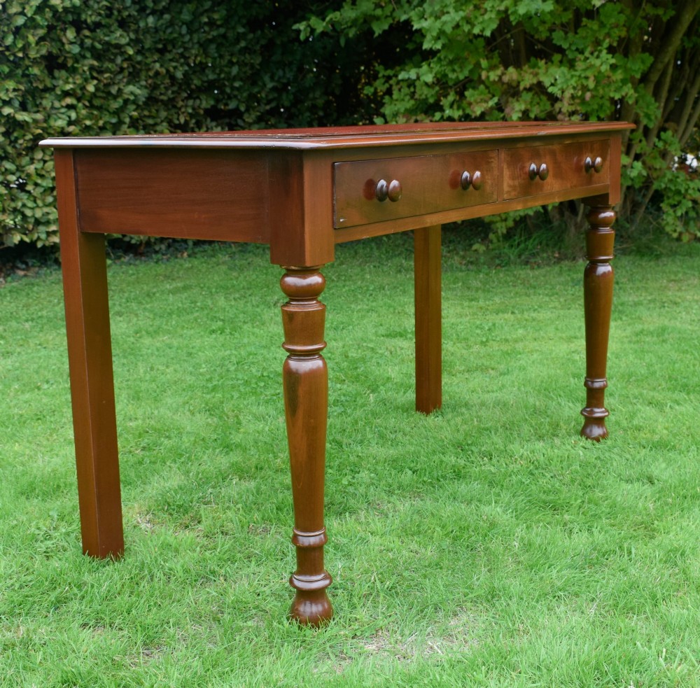 A Victorian mahogany writing table with a red leather inset surface, two drawers with wooden knob handles, turned front legs, and square back legs. View III