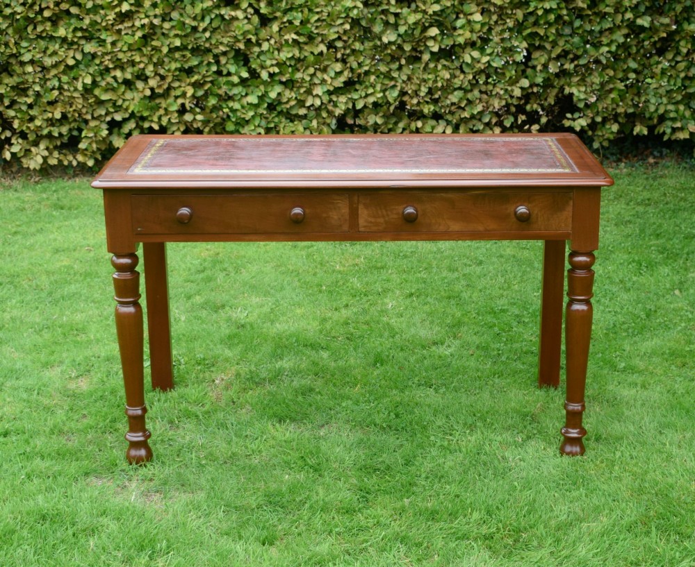 A Victorian mahogany writing table with a red leather inset surface, two drawers with wooden knob handles, turned front legs, and square back legs. View V